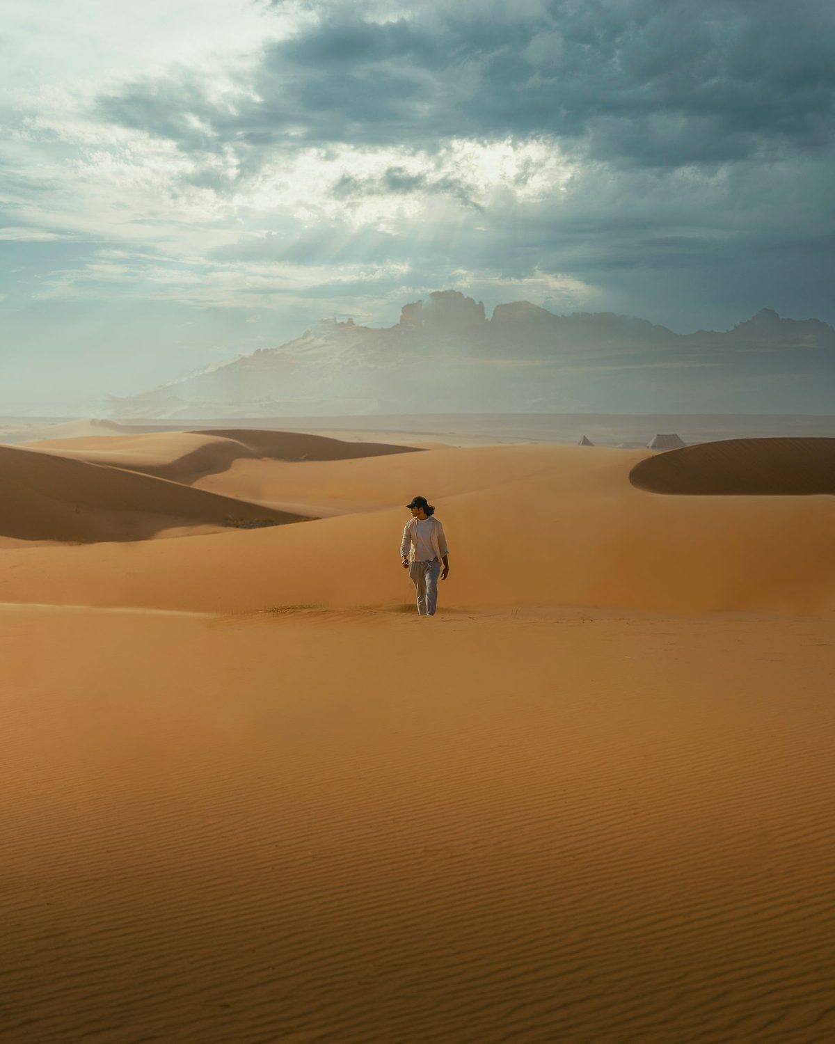 A traveller walking across the vast dunes of Erg Chebbi under a dramatic sky